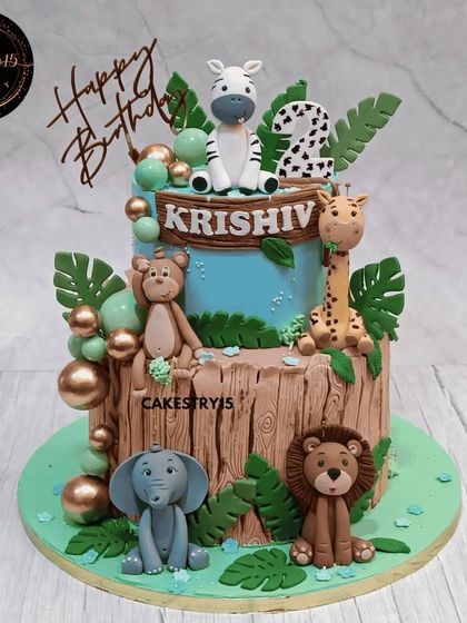 A wild two-tier safari celebration cake for a second birthday. This 5kg chocolate cake has a realistic tree bark texture and is surrounded by a variety of fondant safari animals.