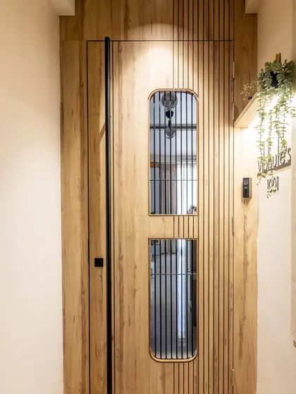 A door is the handshake of a home. This simple, uncomplicated design features a veneer finish and a black metal grill, setting a calm and modern vibe that matches the interiors.