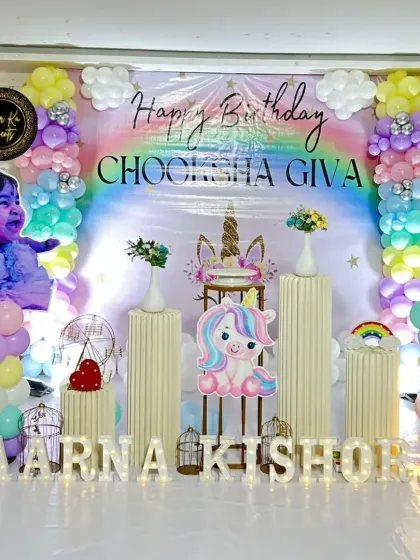 A magical unicorn and rainbow theme for a first birthday. This setup includes a personalized backdrop with the baby's photo, pastel balloon clouds, and multiple unicorn cutouts for a dreamy effect.