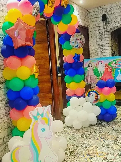 A rainbow and unicorn themed party entrance, with a colorful balloon arch and a unicorn cutout to welcome guests.