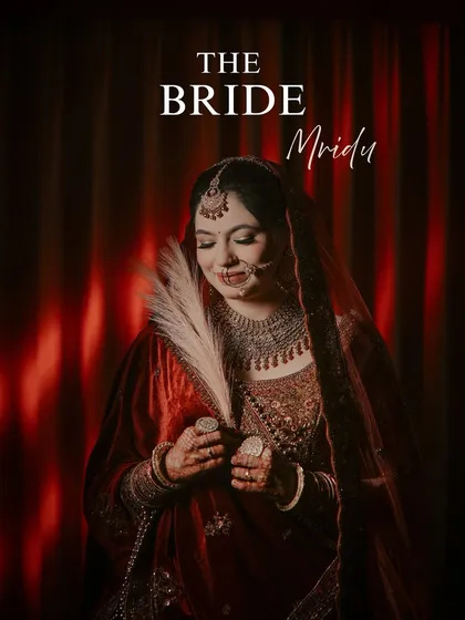 A creative bridal portrait with a feather prop. The bride, in her deep red velvet lehenga, looks serene and divine, creating a unique and artistic image that feels like a painting.