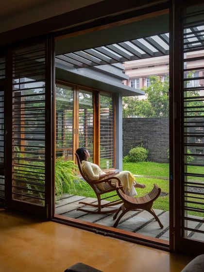 A resident enjoys a moment of peace on a rocking chair, looking out from the living space into the lush private garden.