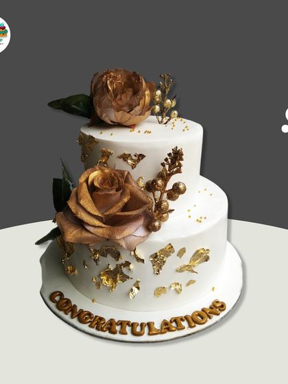 A classic two-tiered cake perfect for any congratulatory event. The design is simple yet stunning, with white buttercream, delicate gold leaf flakes, and two beautiful golden-dusted roses.