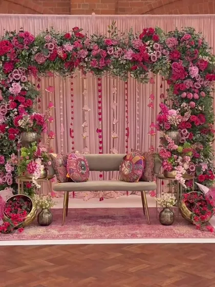 We design elegant and romantic themes for Mehendi ceremonies, like this lush pink floral arch. The setup includes coordinated seating, printed cushions, and traditional decorative umbrellas to complete the look.