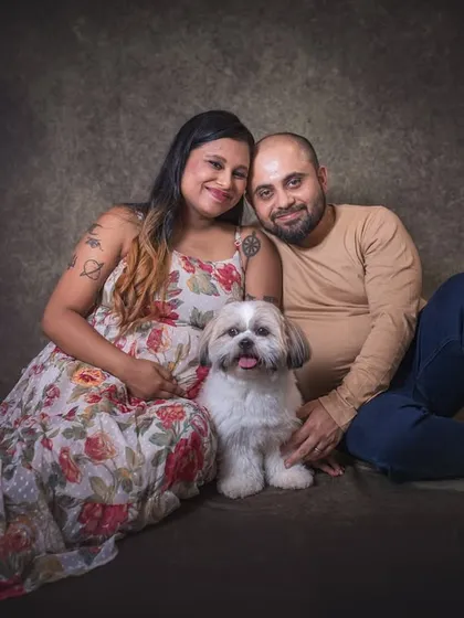 A relaxed and intimate portrait from a studio maternity session. The couple is seated on the floor with their dog, creating a warm and grounded image that highlights their close family connection.