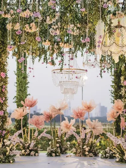 A panoramic view of the reception stage, with a ceiling of hanging florals and a field of oversized paper flowers. The design creates a breathtaking, dream-like landscape with the city skyline as a backdrop.