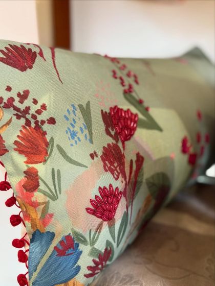 This close-up shows the delicate hand-embroidery on one of our floral cushions. The vibrant red pom-pom trim adds a playful and festive touch, making it a perfect accent piece.
