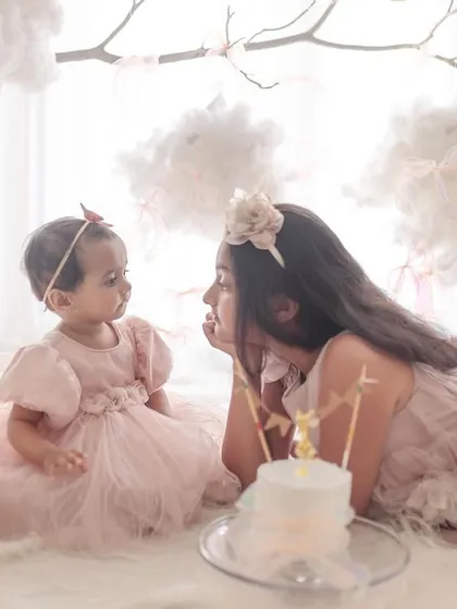 Sisters sharing a moment during a first birthday celebration. The older sister lies down, talking to her baby sister, creating a scene of pure innocence and connection.