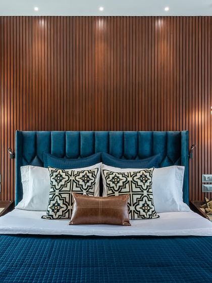 This bedroom showcases a rich and moody aesthetic. The deep blue velvet bed and dark wood fluted wall panel create a luxurious and sophisticated retreat, perfect for unwinding.