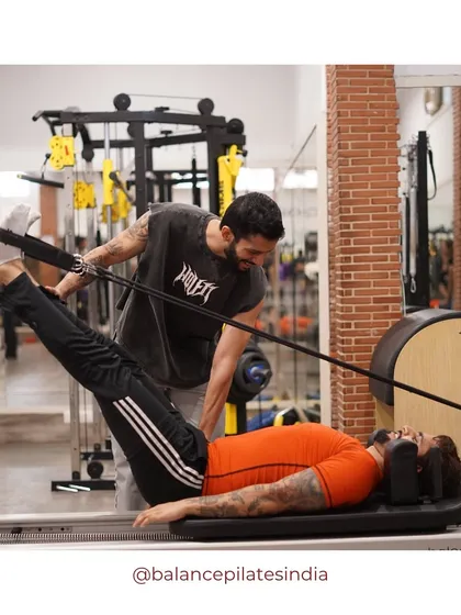 Pilates is for the boys too! Here, a male client gets a hands-on adjustment from a trainer during a leg press on the reformer, showing that men can also benefit from building core strength and flexibility.