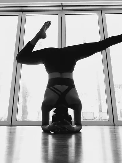Finding new perspectives is a beautiful part of yoga. This artistic shot captures a moment of play and focus in a Salamba Sirsasana (Supported Headstand) variation, silhouetted against the light of the studio windows.
