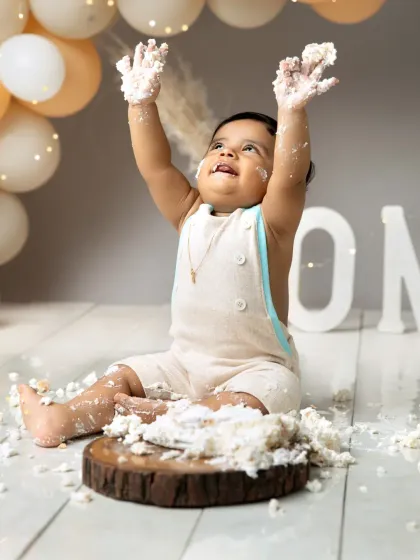 Hands up if you love cake. This little boy is celebrating his first birthday with a joyful throw of frosting, set against a modern backdrop of neutral-toned balloons.