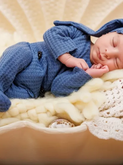 A close-up of a newborn sleeping in a giant seashell. The details of his blue outfit and the soft bedding create a cozy and unique beach-themed photo.