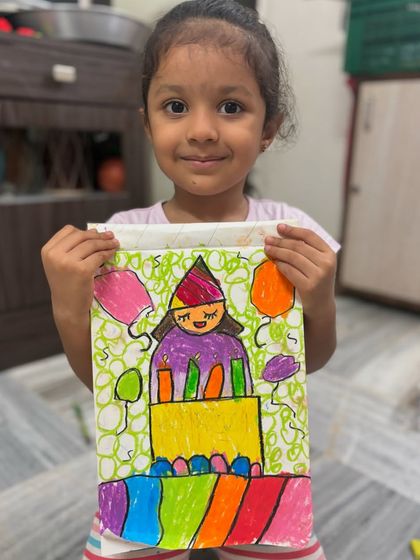 A junior KG student proudly shows her colourful birthday cake drawing. This fun theme allows young artists to play with colours, shapes, and patterns while celebrating a happy occasion.