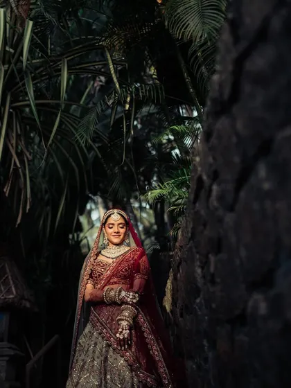 A breathtaking shot of the bride walking through a rustic, stone-walled path, the soft light highlighting her intricate lehenga.
