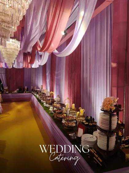 We transform wedding catering into a grand visual experience. Here, a lavish buffet spread is set under elegant pink and lavender drapes, creating a breathtaking dining ambiance for a large wedding celebration.