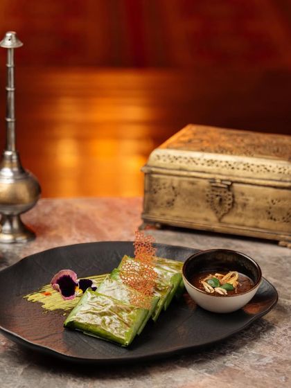 A dish presented with artistry. This banana leaf-wrapped delicacy, served with a rich peanut sauce, is an example of how we combine necessity and art on a single plate.