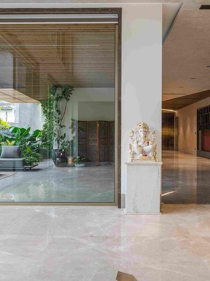 A view from the interior hallway looking out into a lushly planted courtyard. A Ganesha statue marks the threshold, symbolizing a blessed transition from the built environment to the natural one.