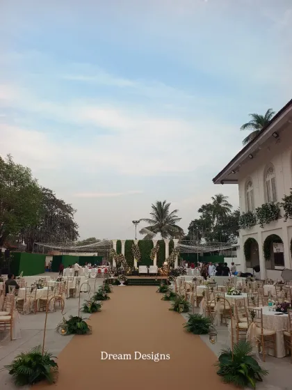 A daytime view of the reception setup, showing the grand scale of the event. The long aisle leads to a large stage against a green backdrop, with seating arranged for all guests to have a perfect view.