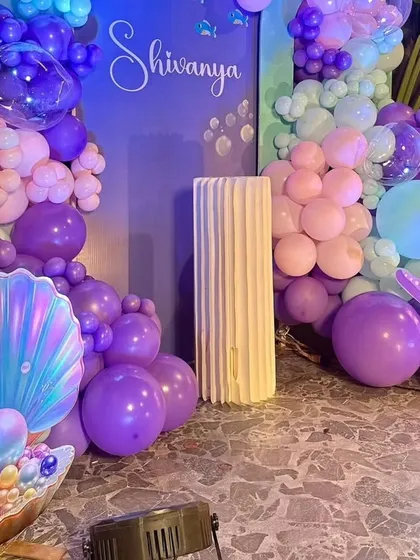 A close-up of a mermaid party's decor, featuring an illuminated clamshell with a pearl and a starfish prop. The purple and teal balloons create an underwater feel.