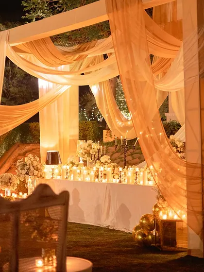 A beautifully draped canopy creates an intimate dining space. The area is lit with dozens of candles, creating a soft, romantic glow for a memorable sangeet dinner.