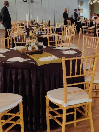 A closer look at a table setting for a formal corporate dinner. The use of dark, rich tablecloths with elegant gold Chiavari chairs and simple centerpieces creates a classic and professional look suitable for any high-profile company function.