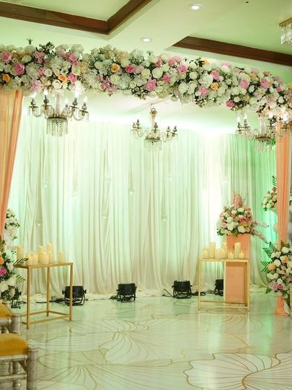 A soft and dreamy stage setup in pastel peach and white. The floral arch and gentle draping create a light and airy feel, perfect for a daytime wedding or an elegant evening reception.