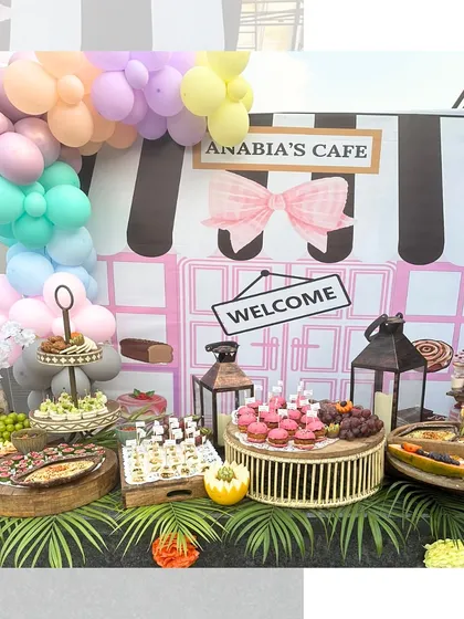A whimsical café themed setup for a child's birthday party. The grazing table features kid friendly treats like cupcakes and fruit platters alongside more sophisticated bites for the adults, all presented in a fun, pastel color scheme.