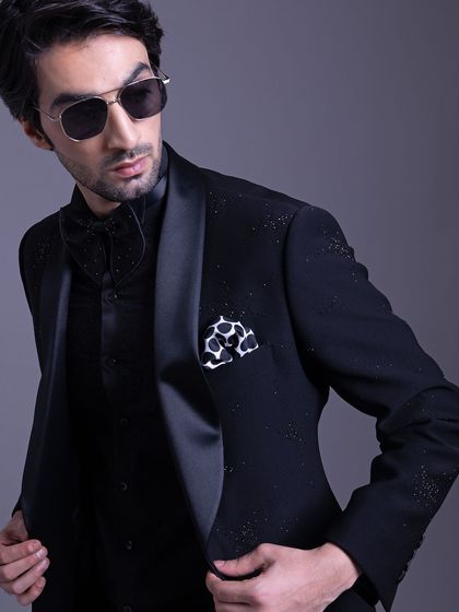 A three-piece evening look in all black, featuring a subtly embellished jacket. The addition of a patterned pocket square adds a pop of contrast.