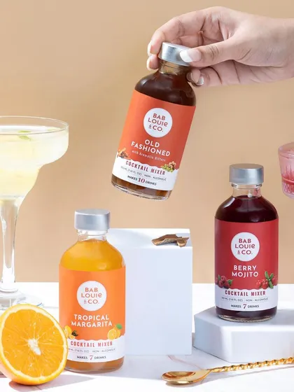 A vibrant group shot of cocktail mixers for Bab Louie & Co. The styling with fresh fruit and prepared drinks communicates the product's use and flavor profiles, creating a bright, appealing image for beverage brands.