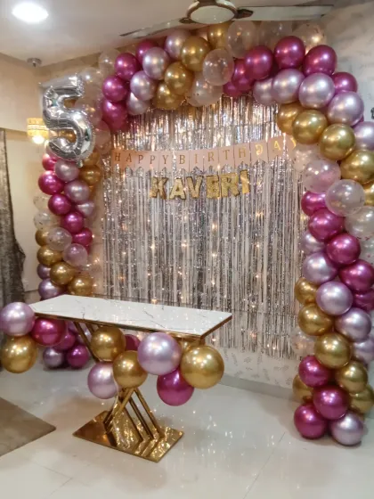 While we specialize in anniversaries, our balloon decoration skills are perfect for any celebration. Here is a beautiful balloon arch we designed for a 5th birthday party, using a theme of pink, gold, and transparent balloons with a silver foil curtain and a number '5' balloon.
