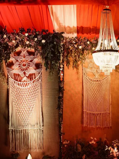 We specialize in creating unique themes, like this autumn-inspired decor. The combination of warm red drapes, intricate macrame wall hangings, and a classic chandelier creates a cozy, bohemian vibe perfect for an intimate gathering.