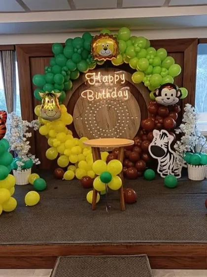 A jungle-themed birthday stage with a wooden backdrop, neon sign, and balloon columns with animal foils.