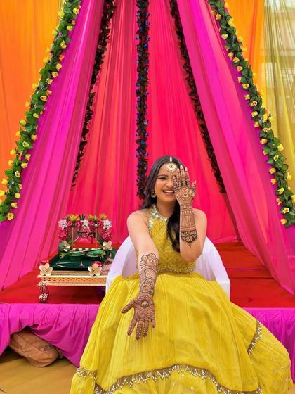 A happy bride-to-be at her mehndi ceremony, set against a colorful backdrop.
