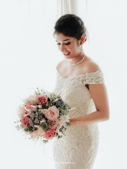 A beautiful portrait of the bride in her off-the-shoulder lace gown, looking down at her pastel bouquet with a gentle smile.