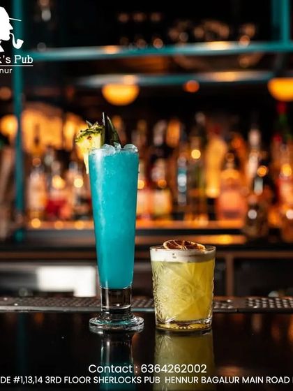 Two of my signature cocktails sitting on the bar. The tall, electric blue drink and the frothy, citrusy short drink showcase the different styles and flavor profiles you can explore here.