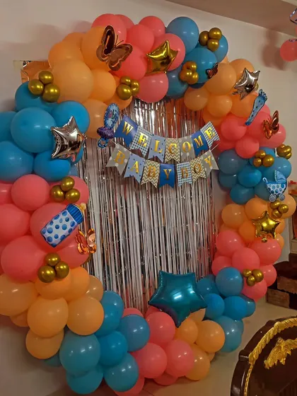 A 'Welcome Baby Boy' ring decoration in orange and blue, with a silver fringe curtain and butterfly and star accents.