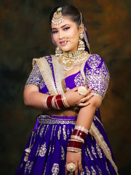 A stunning bridal portrait in a royal purple lehenga, showcasing a full set of jewelry including the nath (nose ring) and maang tikka.