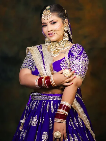 A vibrant purple bridal lehenga paired with classic gold jewelry. The makeup is kept glamorous with a smokey eye and a neutral lip to balance the bold color of the outfit.