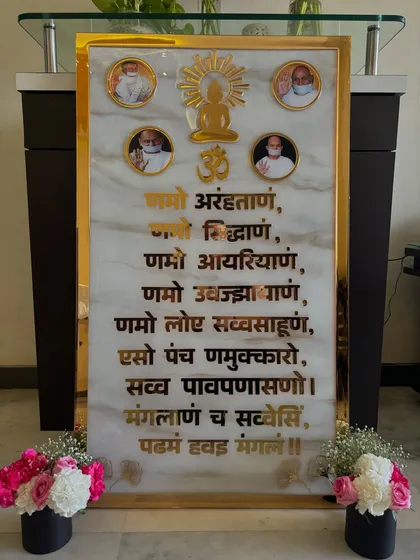 A full view of the large Navkar Mantra frame installed in a client's home. The piece is flanked by flowers, showing how it can become the focal point of an entryway or prayer room.