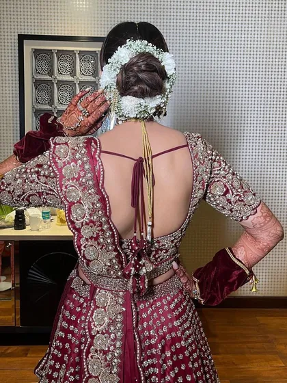A back view of a bridal updo for a bride in a rich maroon lehenga. The bun is neatly wrapped with a gajra of fresh white flowers, creating a beautiful contrast and a classic wedding look.