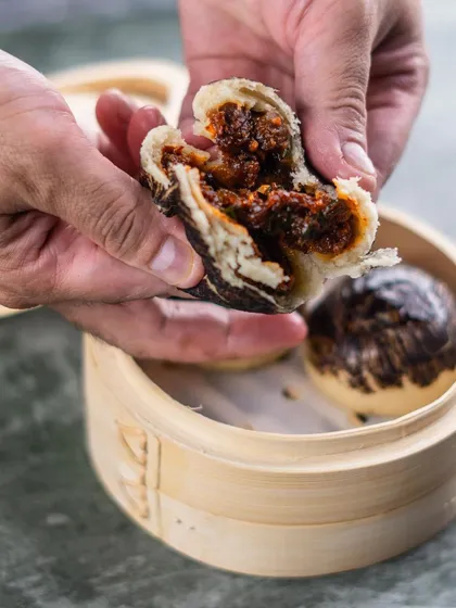 The reveal. A Char Siu Pork Bao is broken open to show the savory, saucy pork filling, a fan-favorite from our pan-Asian menu.