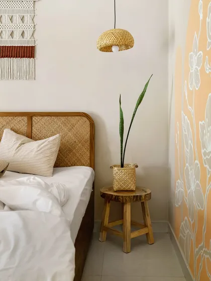 A detail of the bedside at Unallome. A simple wooden stool, a woven planter, and a snake plant add touches of rustic charm. The design embraces minimalism and handcrafted elements to promote a sense of mindful living.