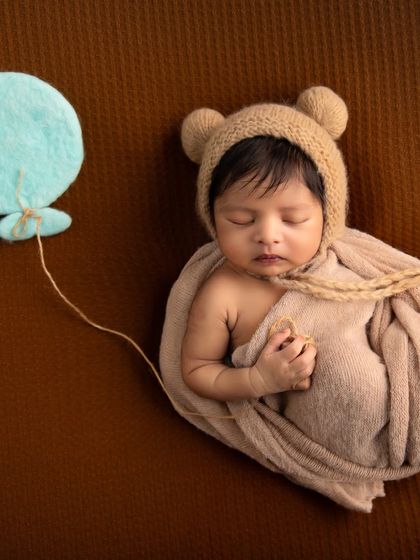 A simple and sweet themed shot. The baby, dressed as a little bear, holds the string of a felt balloon, creating a light and whimsical image against a textured brown backdrop.