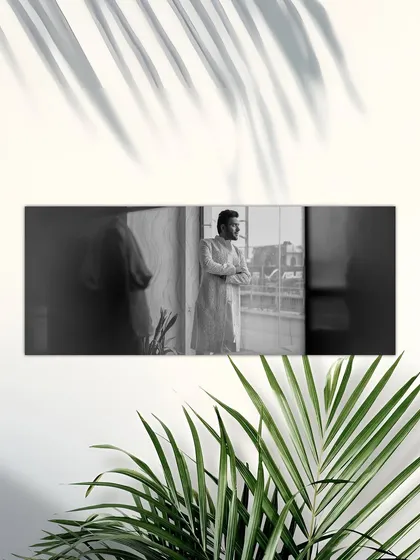 A thoughtful black and white portrait of the groom looking out a window. The natural light and shadows create a contemplative and cinematic mood.