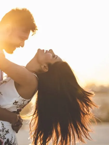 Pure joy captured during a golden hour sunset. The couple shares a spontaneous, laughing moment, with the warm light creating a beautiful, romantic flare that highlights their connection.