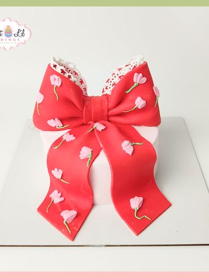 A cake wrapped like a present, because every celebration is a gift. This design features a large, beautiful red bow with delicate floral details.