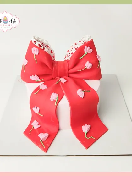 A cake wrapped like a present, because every celebration is a gift. This design features a large, beautiful red bow with delicate floral details.