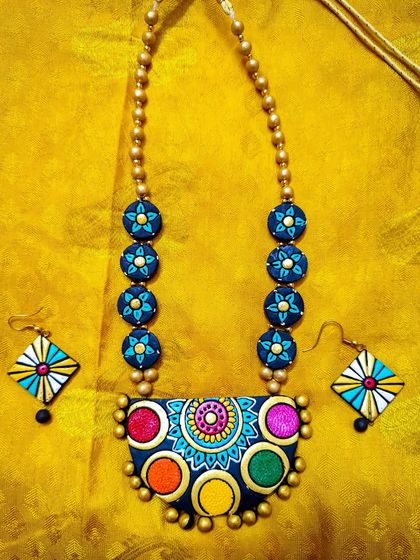 This multi-colored necklace features a unique pendant with five distinct color circles. The design is modern and playful, and it comes with kite-shaped earrings.