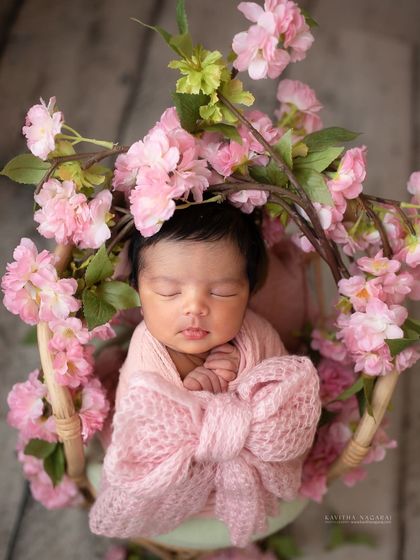 Another view of a newborn girl wrapped in a pink bow, surrounded by flowers. The composition feels like she is a precious gift, beautifully presented.